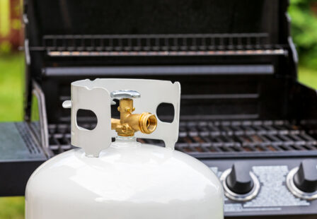 Close-up of a propane tank valve and brass connector in front of an outdoor gas grill